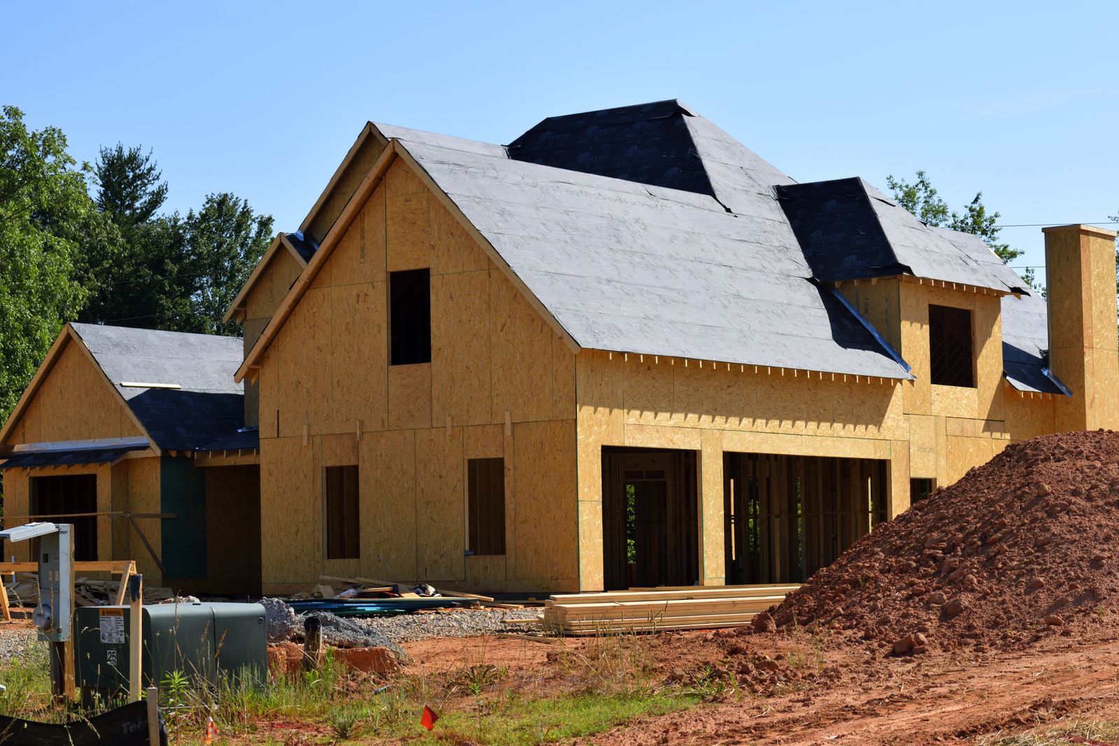 A house shell sheathed in fresh plywood on a graded red-clay lot