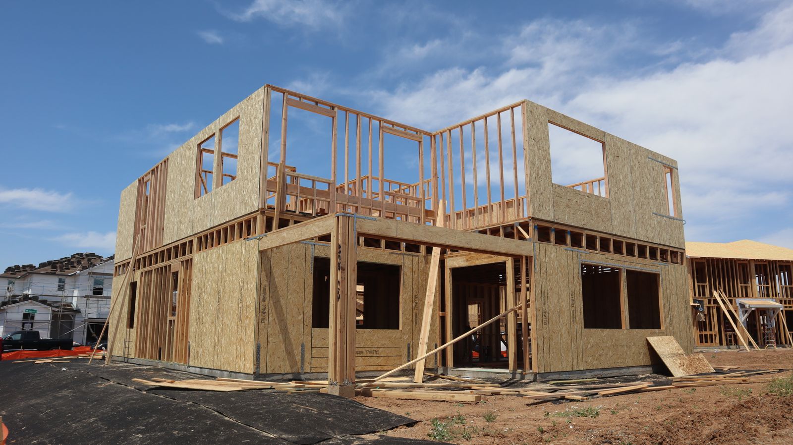 A two-storey timber house frame standing under a clear blue sky