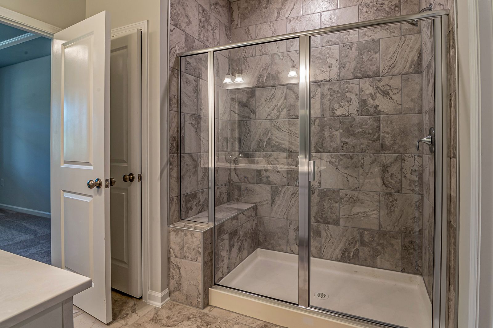 A remodeled bathroom with a glass-door walk-in shower and gray tile