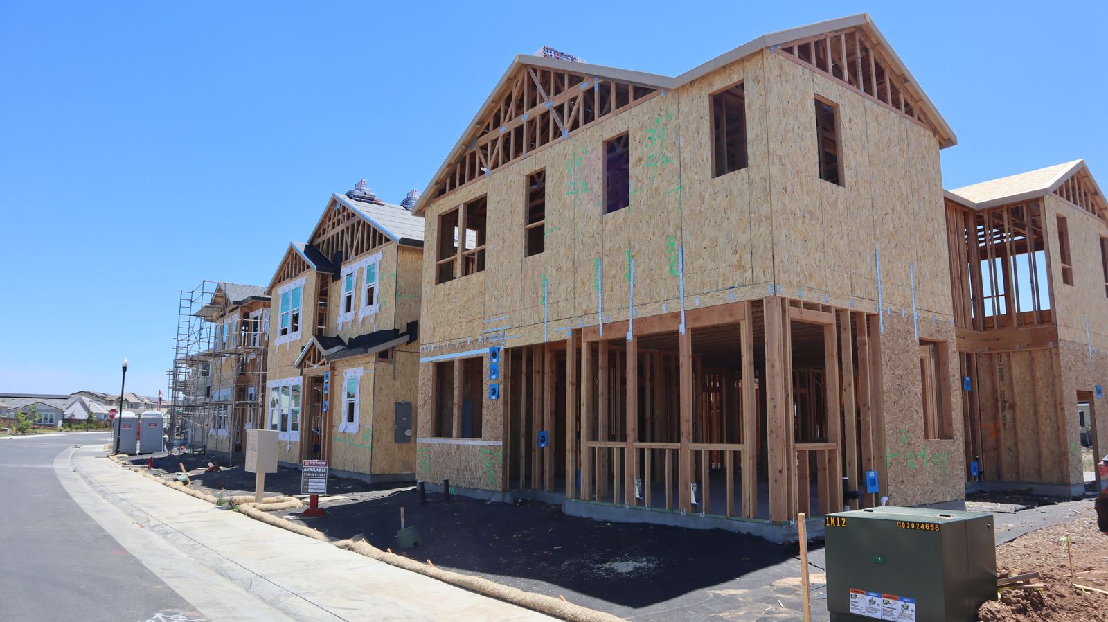 A row of newly framed houses with fresh sheathing under a blue sky